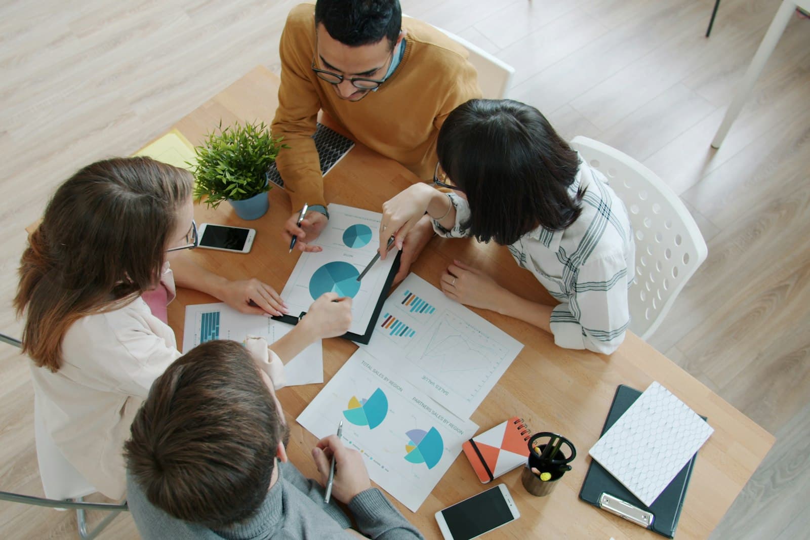 Quatre collègues réunis autour d’une table de travail, vus de dessus, annotant ensemble des graphiques imprimés.